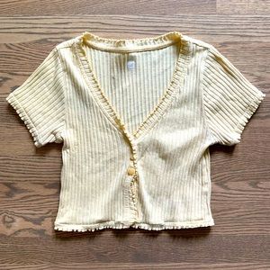 Yellow crop top with ruffled edges and two little buttons on the front